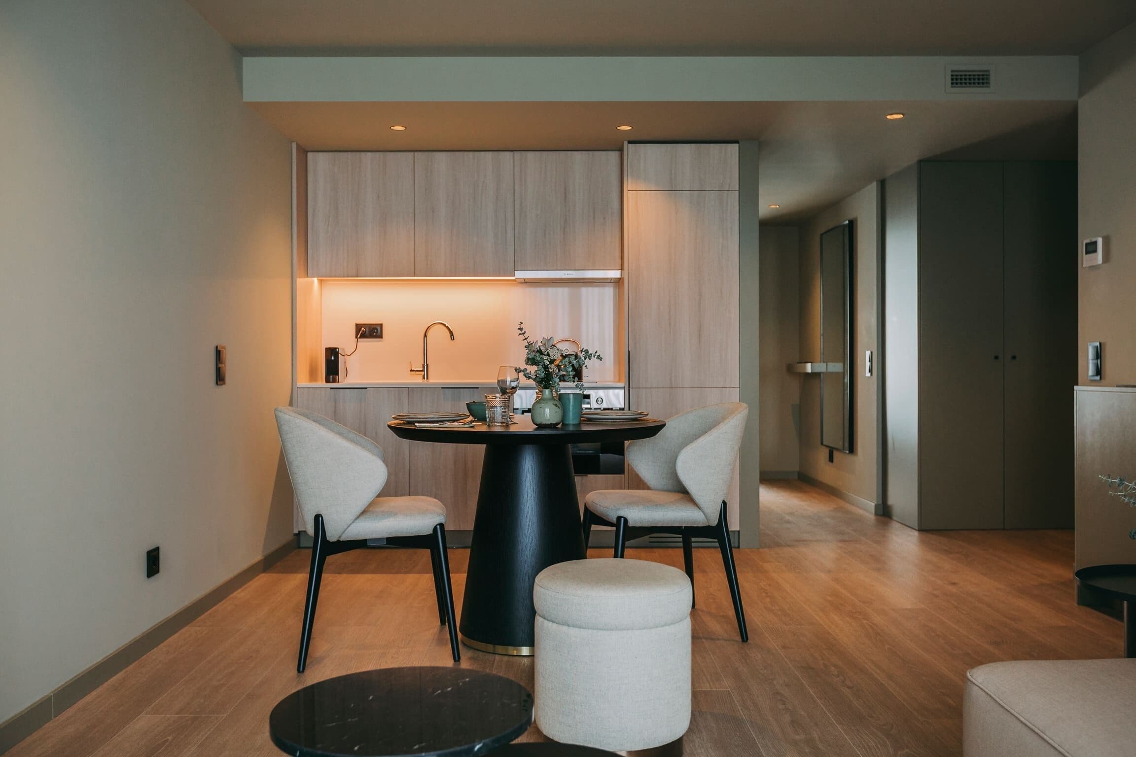 A modern kitchen with wooden cabinets, a round dining table with chairs, and a small round table with a black top.