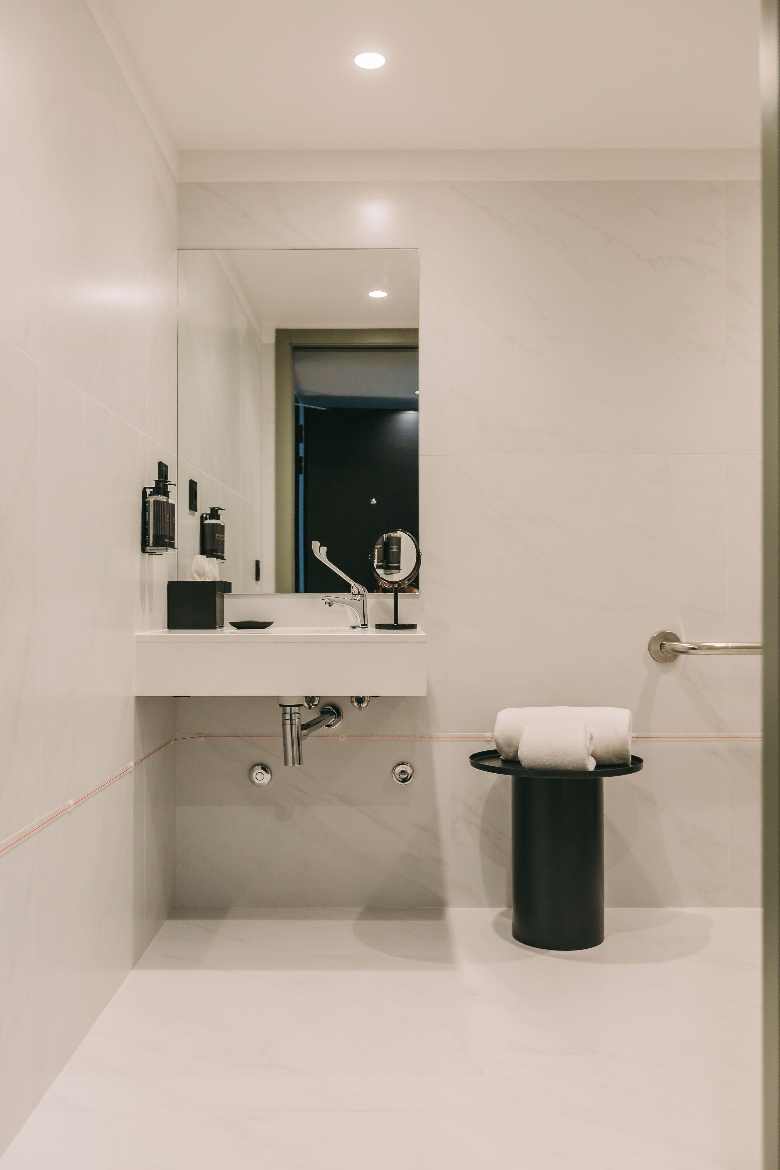 Et moderne badeværelse med en hvid vask, spejl og et sort toilet.