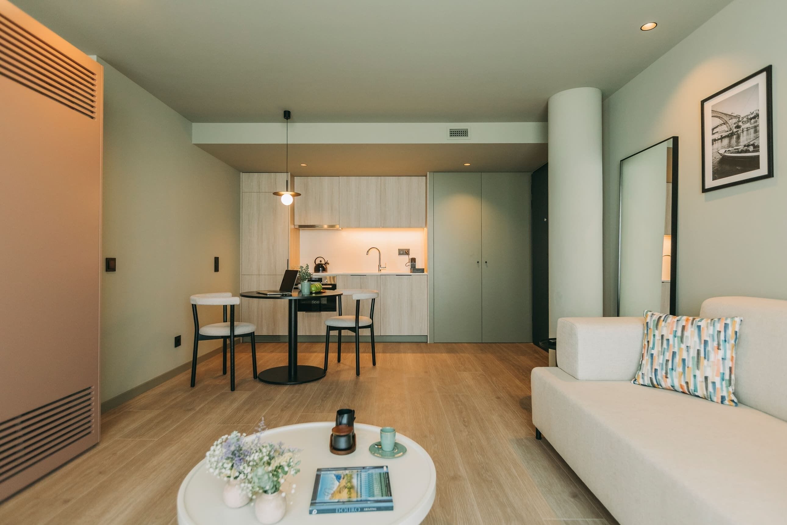 Uma sala de estar moderna com um sofá, uma mesa de centro com objetos decorativos e um espaço de jantar com cadeiras e uma mesa.