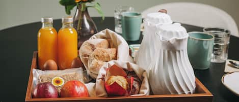 Un plateau en bois contenant des aliments pour le petit-déjeuner, notamment du pain, des viennoiseries, des fruits et des bouteilles de jus.