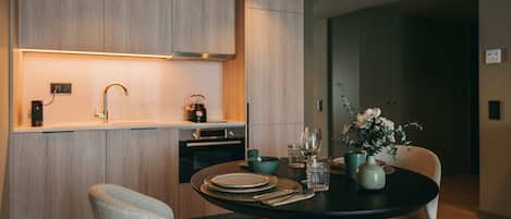 Une cuisine moderne avec des meubles en bois, un four encastré et un coin repas agrémenté d’une table ronde pour deux personnes.