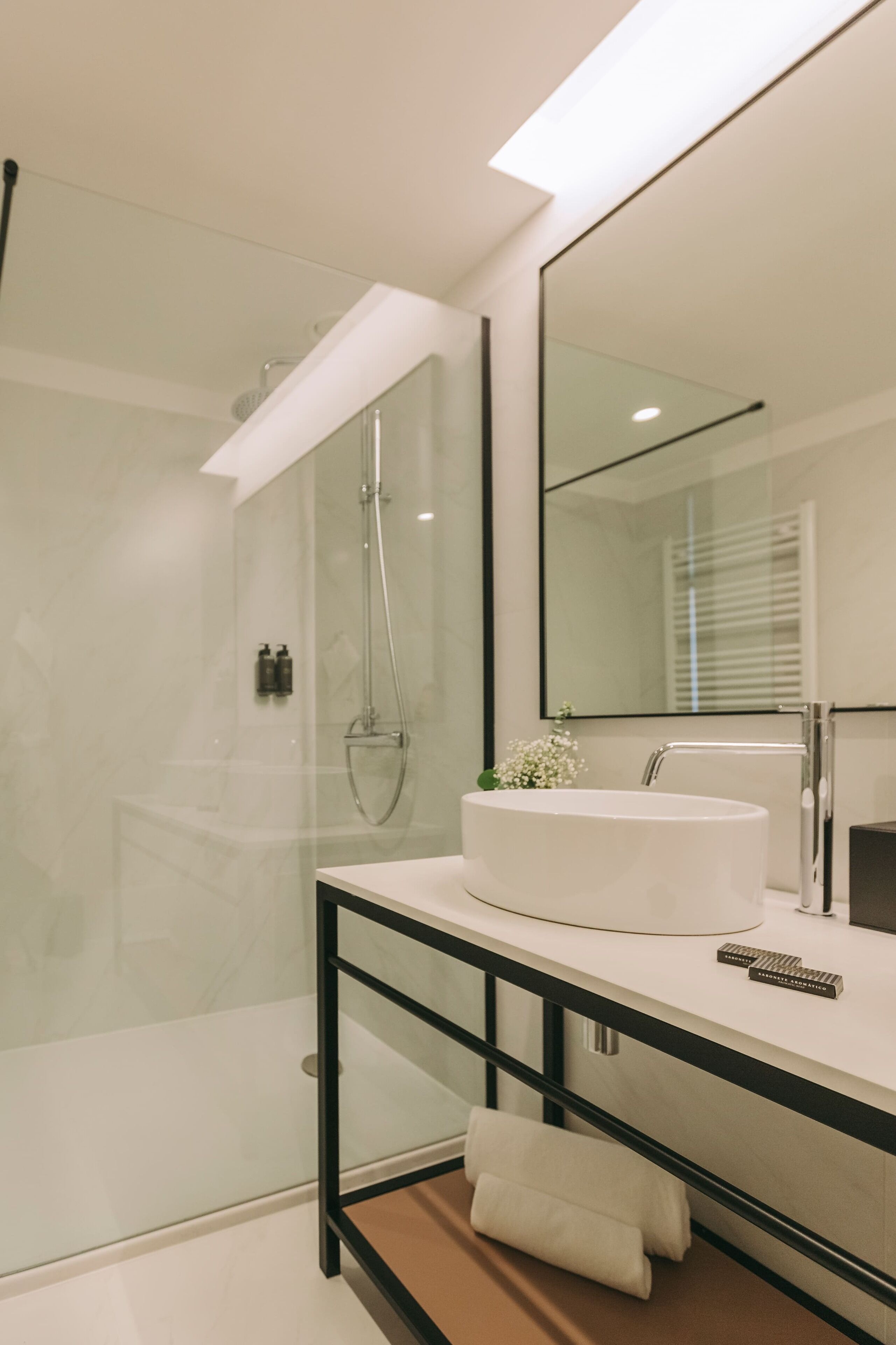 Un baño moderno con cabina de ducha de vidrio, un lavabo blanco y un espejo grande.