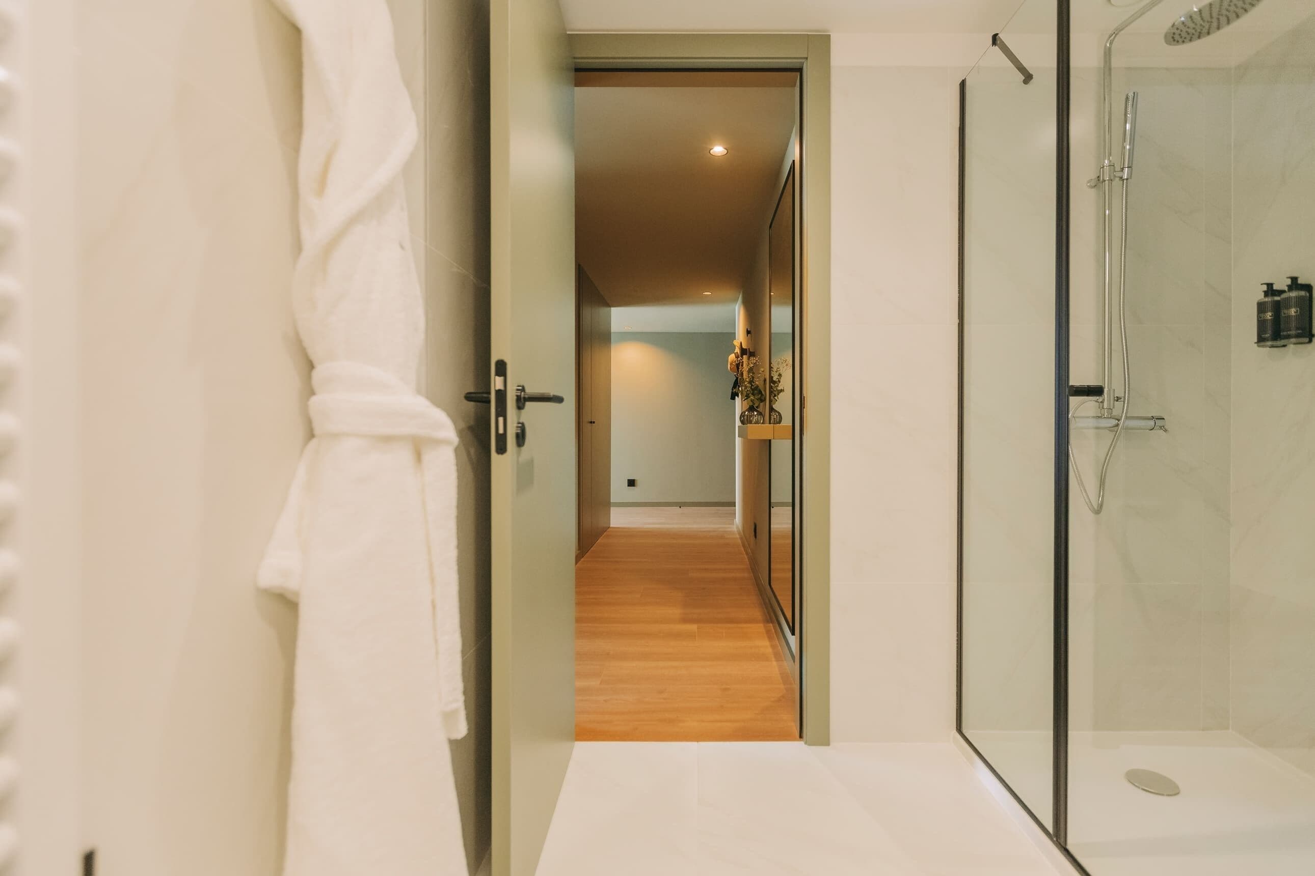 Un bany modern amb una cabina de dutxa de vidre, un terra de fusta i una banyera blanca.