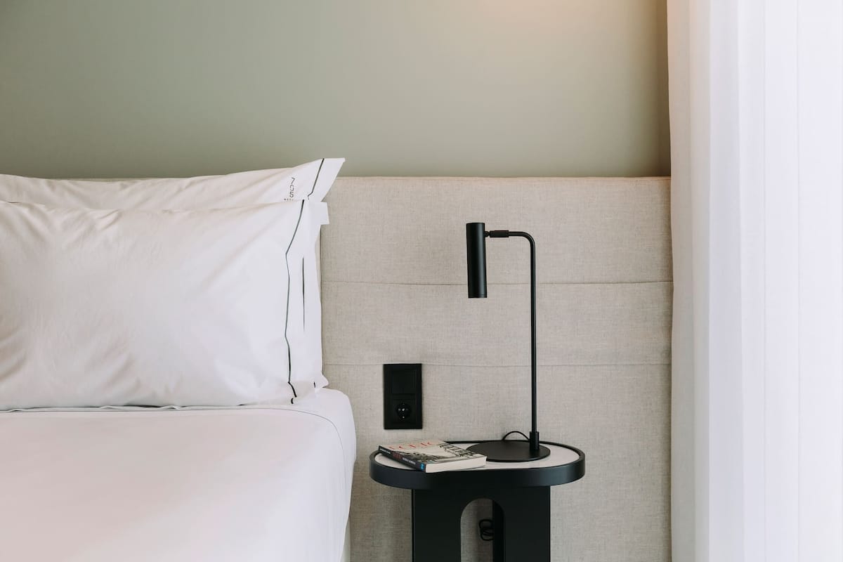 A neatly made bed with white linens, a black bedside table with a lamp, and a book.
