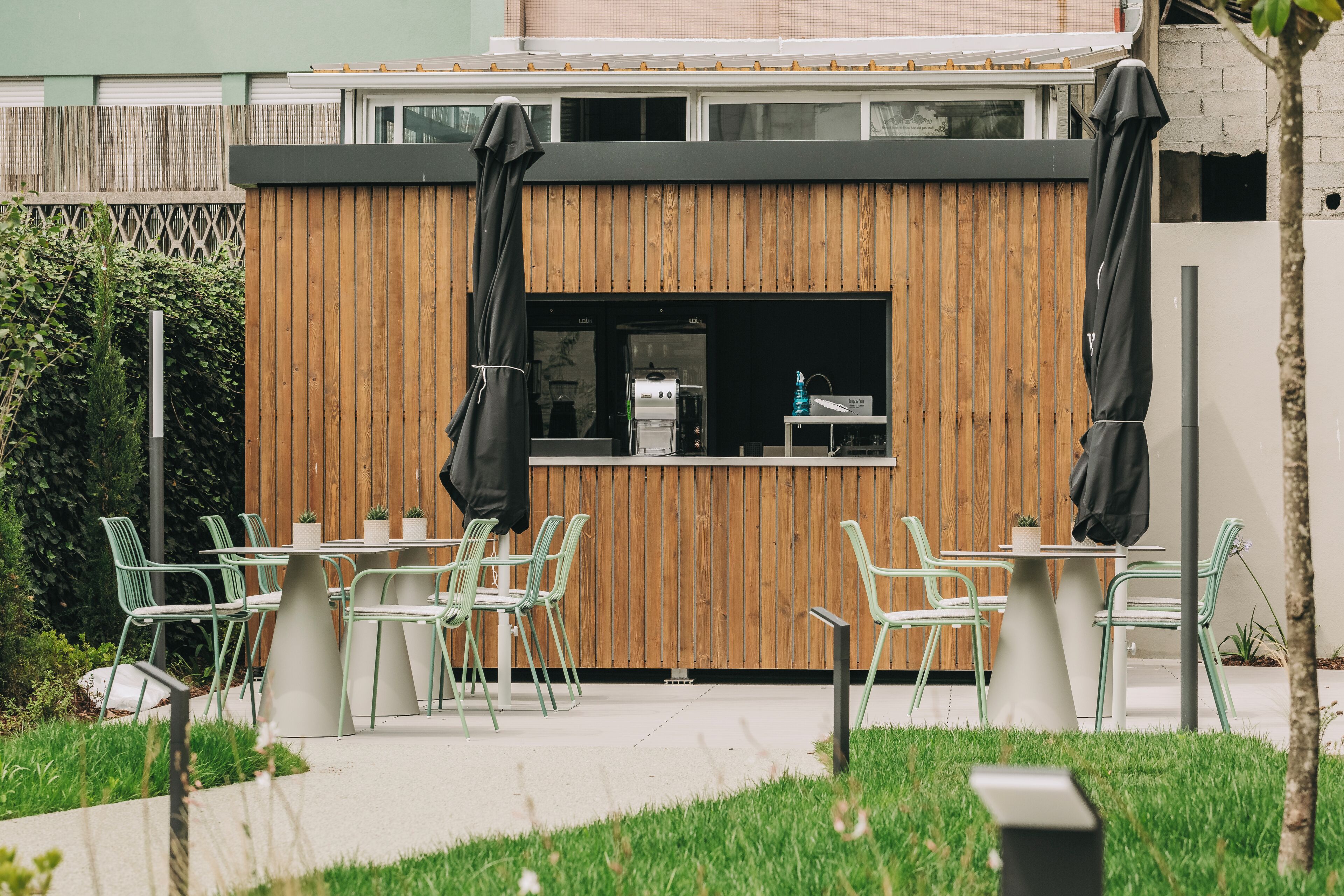 Un espace extérieur aménagé en terrasse, avec une cloison en bois, des chaises vertes et un coin barbecue.