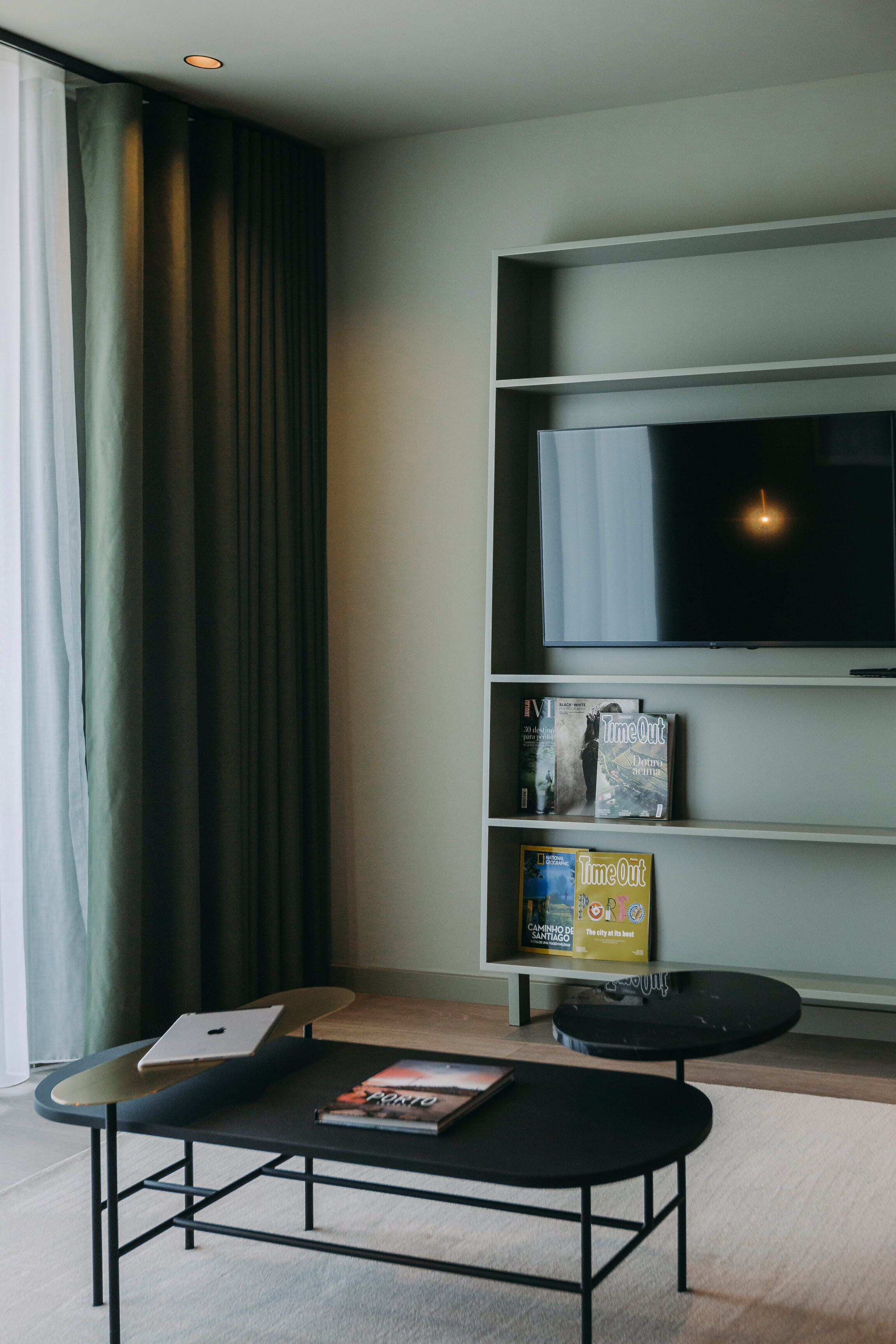 Ein modernes Wohnzimmer mit Flachbildfernseher, einer Couch, einem Couchtisch und einem Bücherregal mit Büchern.