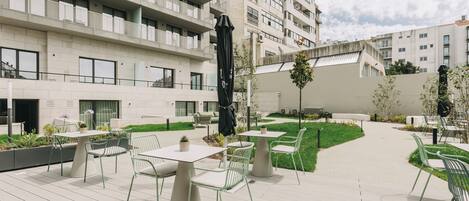 A courtyard with outdoor seating, a large black sculpture, and a building with multiple balconies.