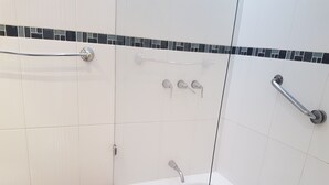 Ein Badezimmer mit weißen Fliesen, einer Badewanne und einem Duschbereich mit Haltegriffen.