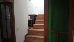 Eine Holztreppe mit einer grünen Glastür, die zu einem Raum mit weißer Wand und einer Leuchte führt.