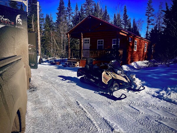 Une cabane en rondins avec une motoneige garée devant.