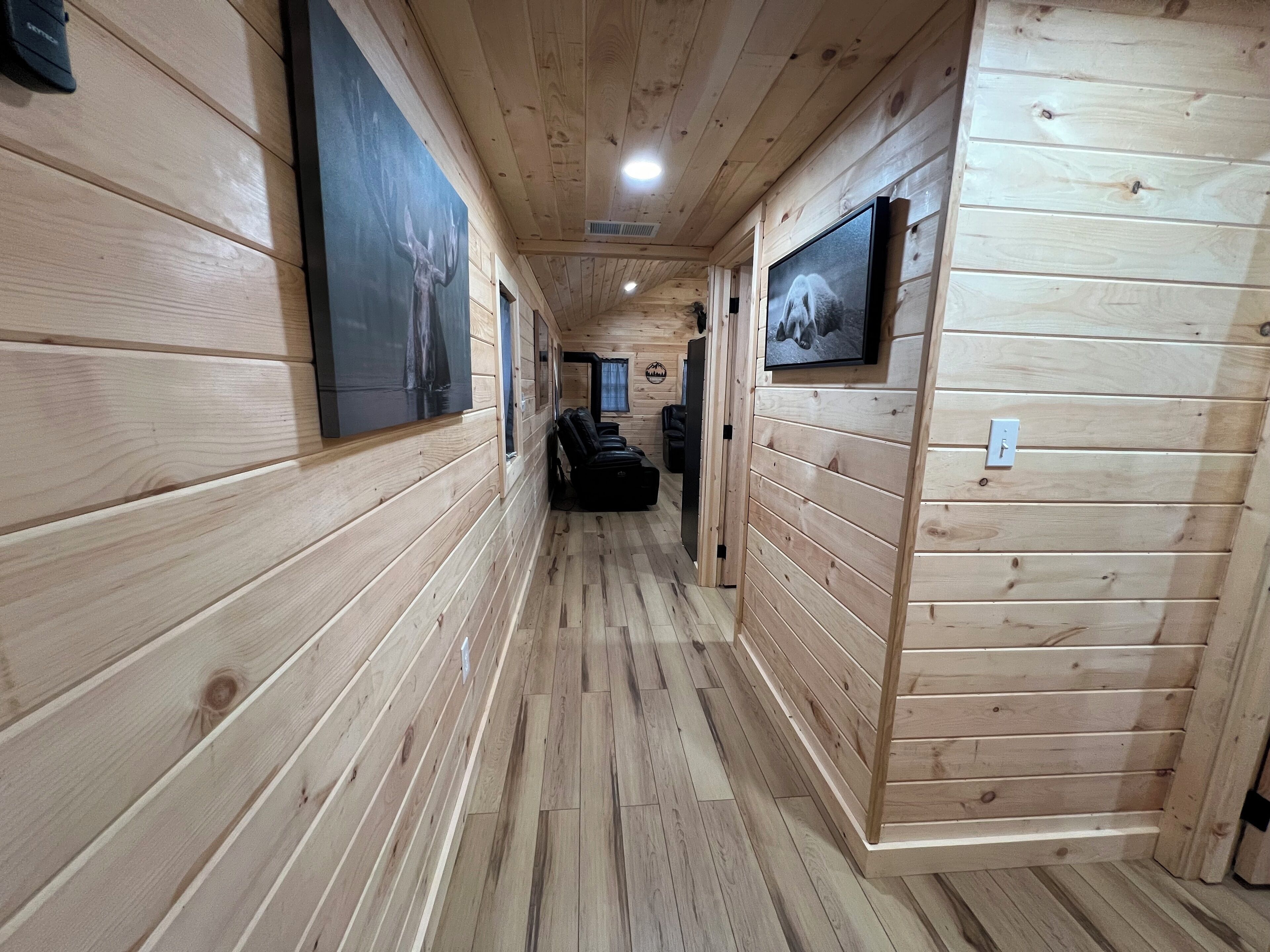 A wooden hallway with framed pictures on the walls, a ceiling light, and a door at the end.