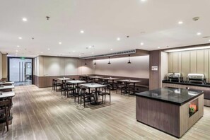 A modern hotel dining area with multiple tables and chairs, a central island with a counter, and a kitchen area in the background. - HanTing Hotel (Shenzhen Xili Subway Station) (Shenzhen)