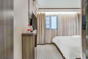Una habitación de hotel con una cama, una mesita de noche con una botella y una taza, una ventana con cortinas y un aire acondicionado de pared.