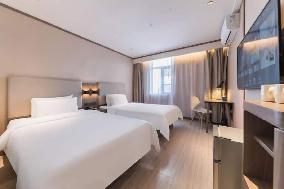 A hotel room with two beds, a desk, a chair, a TV, and a window with curtains.
