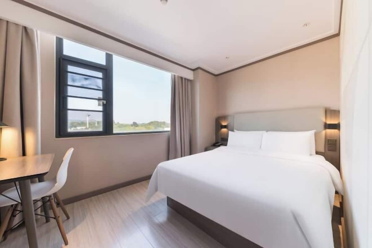A hotel room with a bed, a desk, and a window.