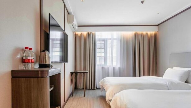 Et hotelværelse med to senge, et fjernsyn, en minibar og et vindue med gardiner.
