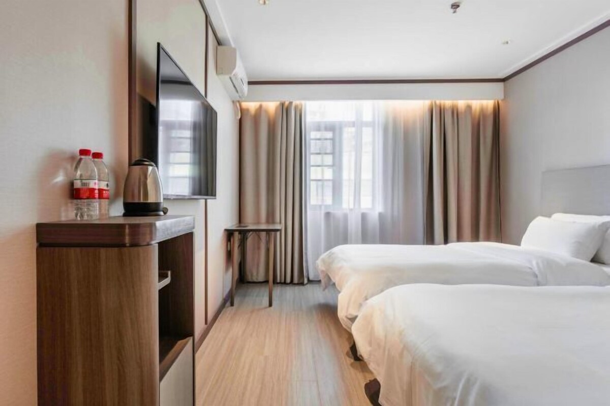 Habitación de hotel con dos camas, televisor, minibar y ventana con cortinas.
