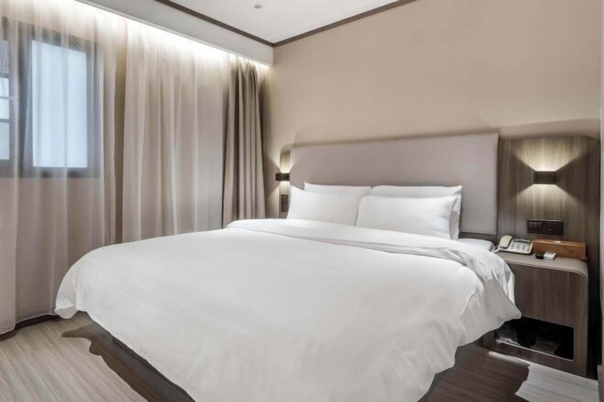 Una habitación de hotel moderna con una cama grande, una mesita de noche con teléfono y una lámpara fijada a la pared.