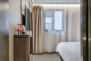 Una habitación de hotel con cama, televisor sobre un soporte de madera y ventana con cortinas.