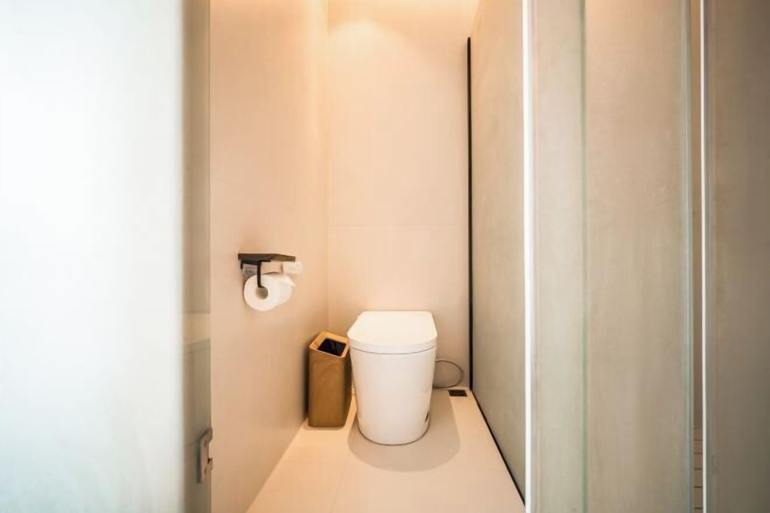 A small, modern bathroom with a toilet, a trash bin, and a toilet paper holder on the wall.