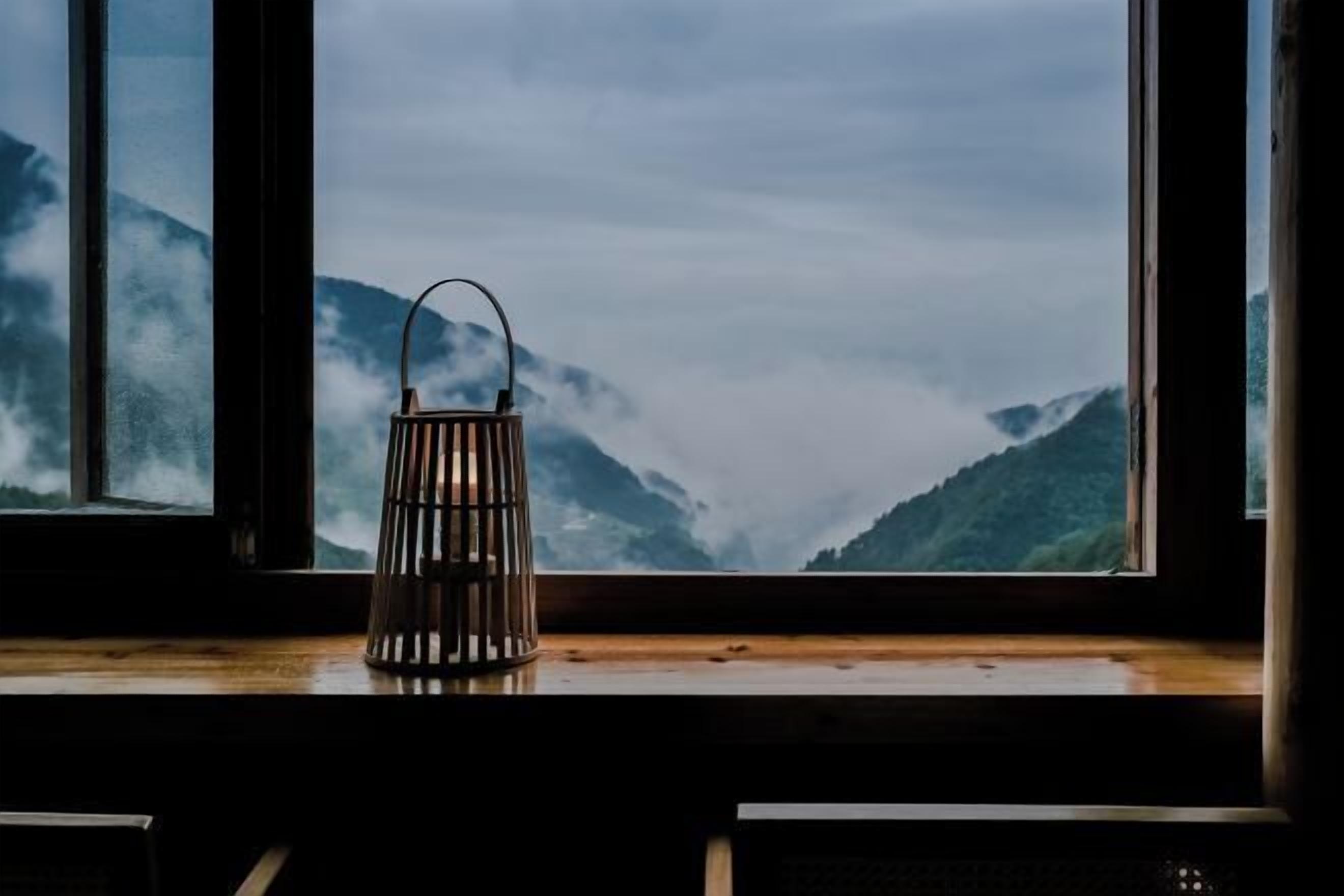 A lantern on a windowsill with a view of mountains and clouds.