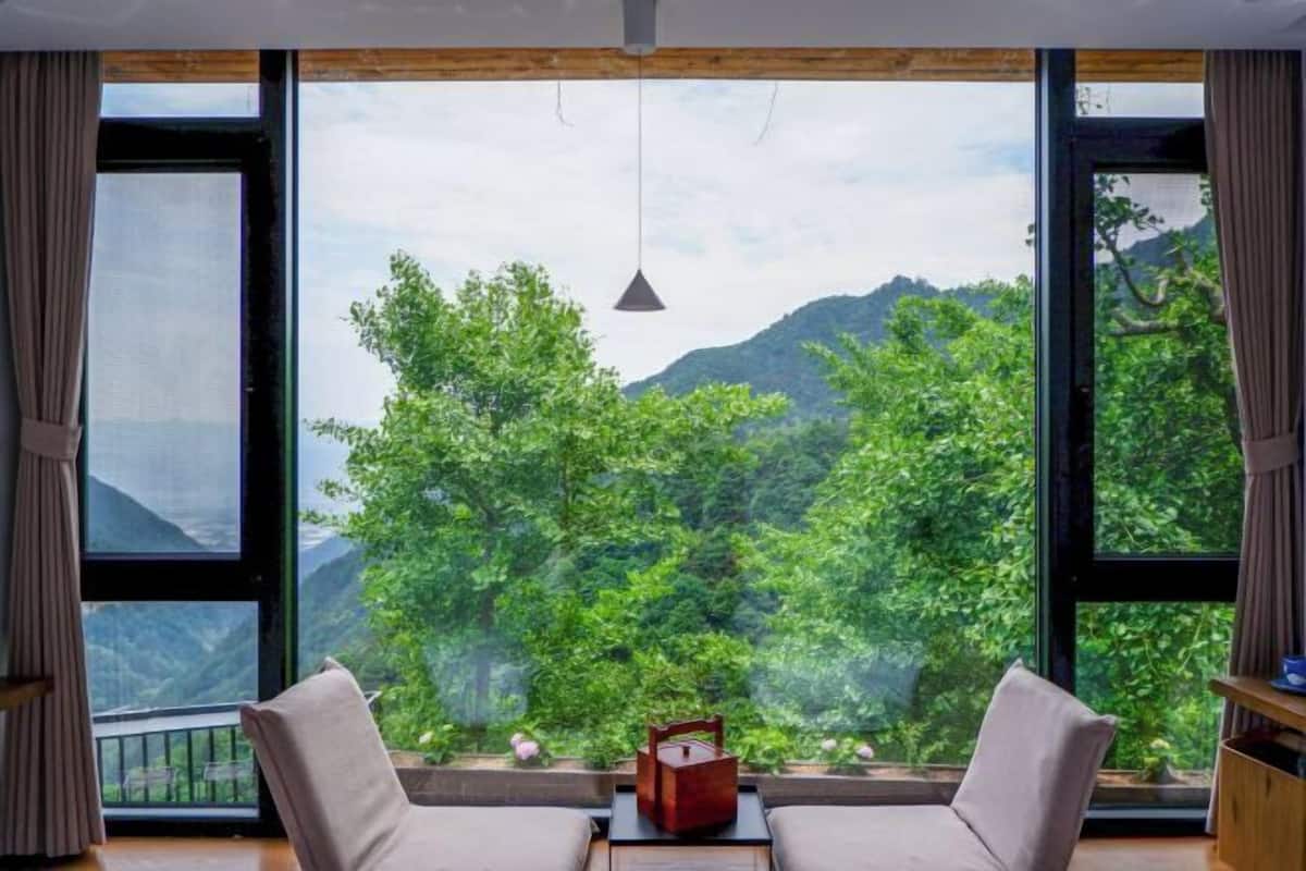 A room with large windows, a hanging light fixture, and a view of green hills.