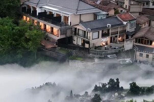 Un edificio residencial de varios pisos con balcones, un patio interior y zonas arboladas envueltas en niebla.