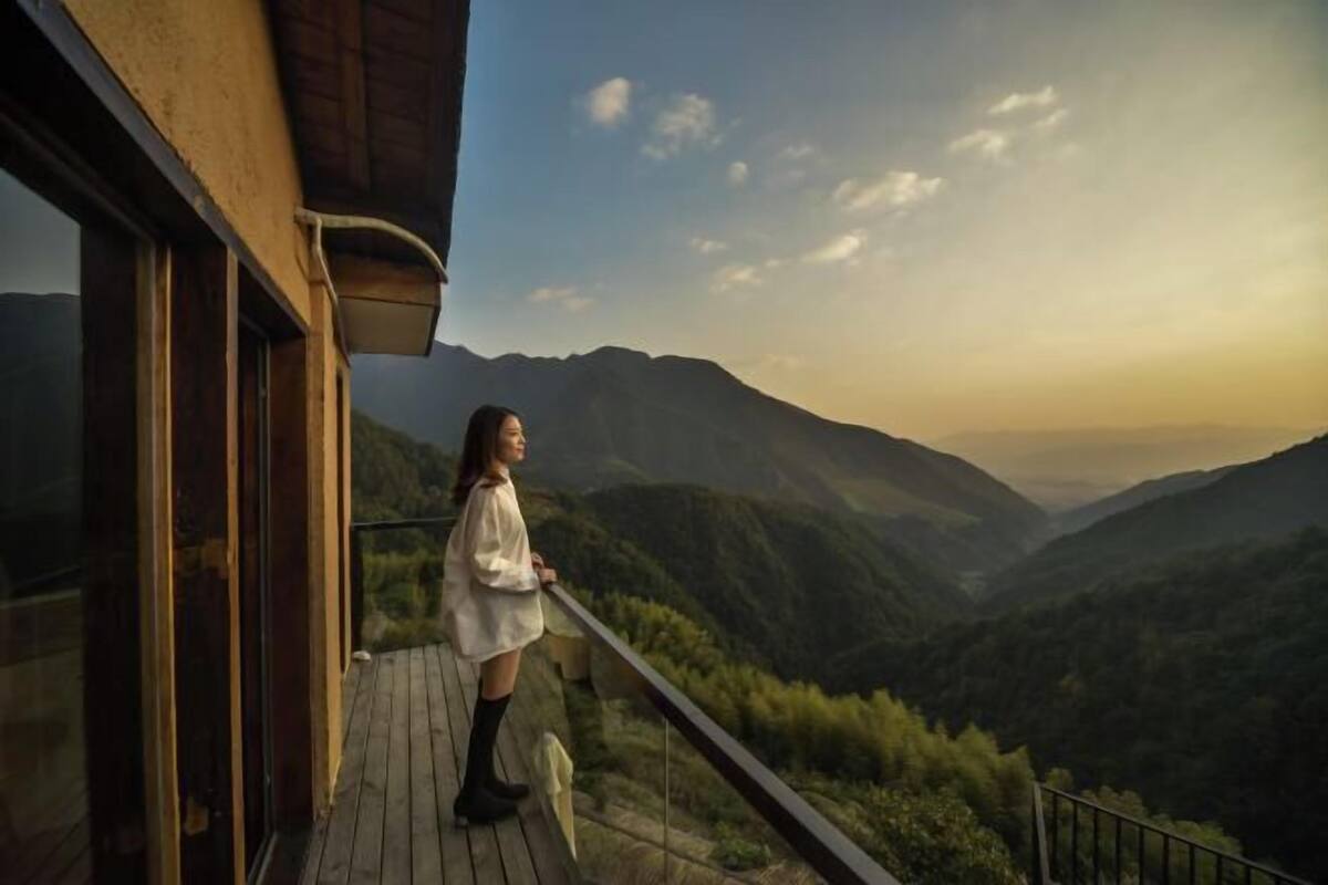 A person standing on a balcony overlooking a mountainous landscape.