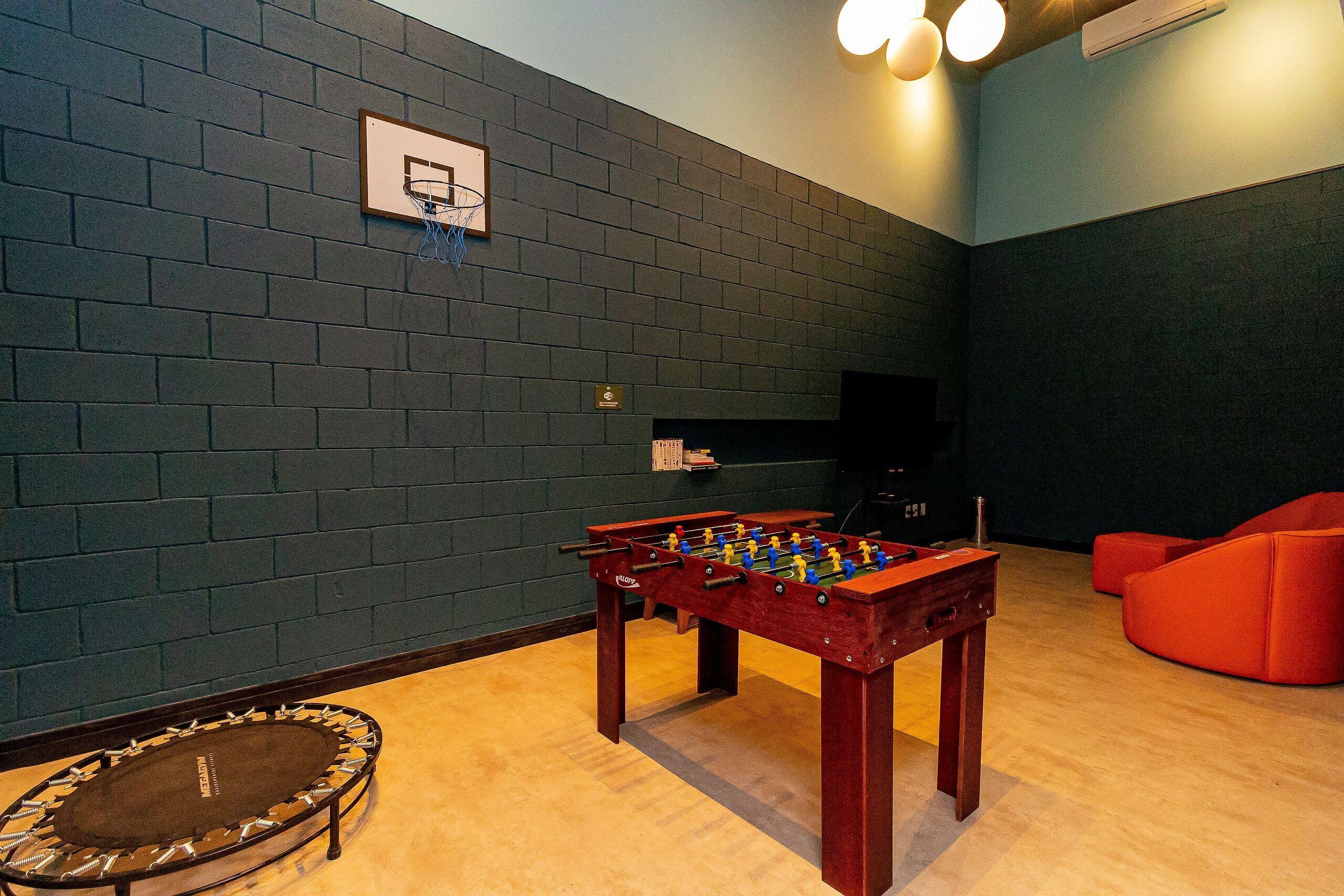 Een kamer met een tafelvoetbaltafel, een trampoline en een basketbalring.