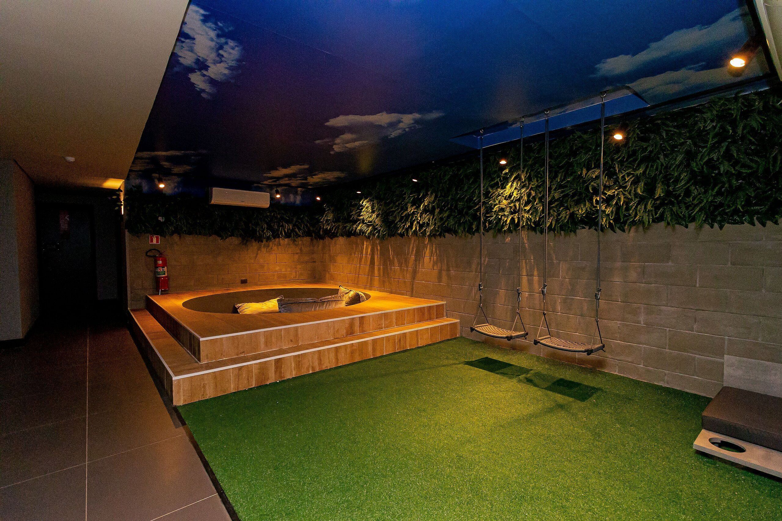 A modern indoor pool area with a hot tub, artificial grass, and a swing chair.