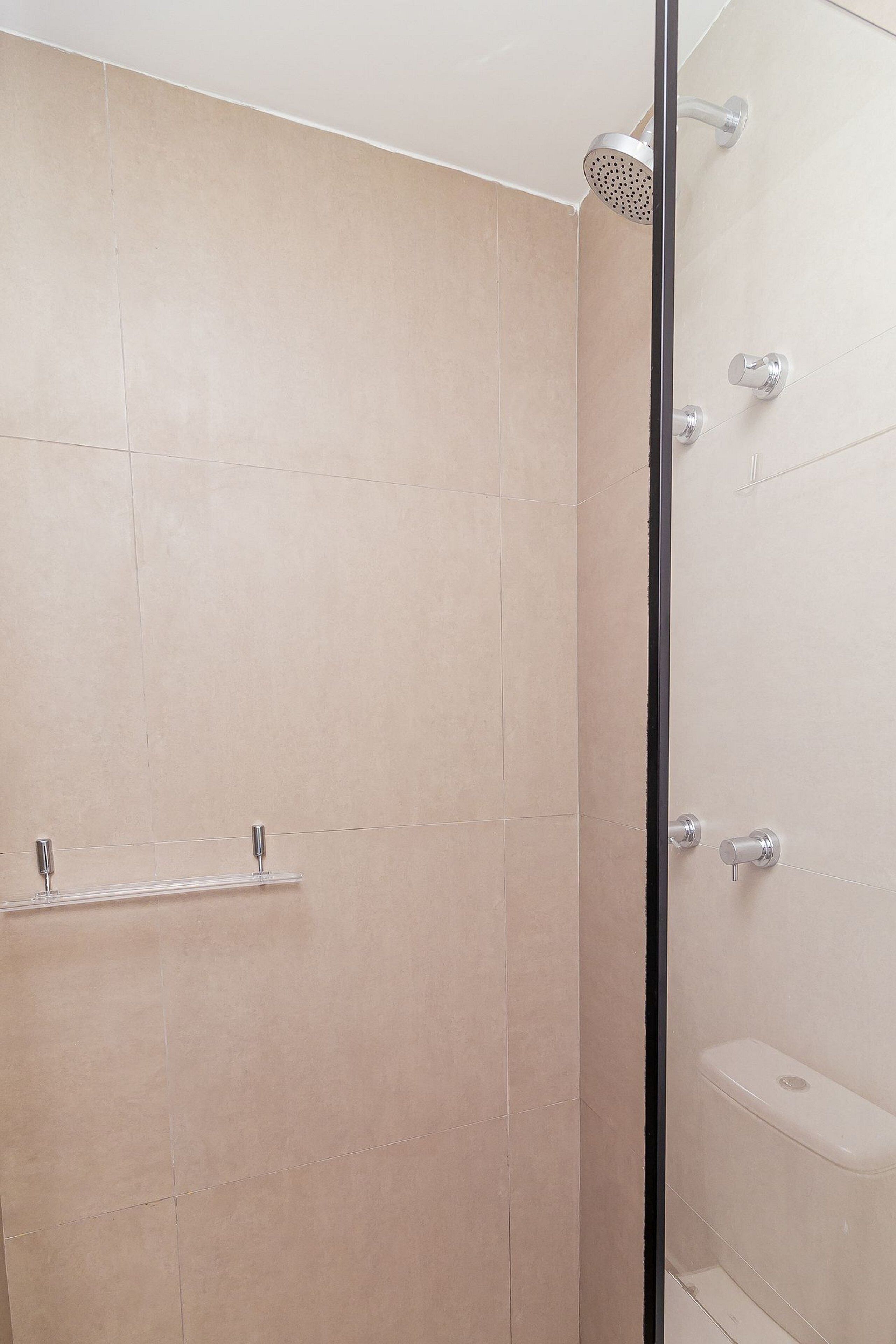 Un baño moderno con baldosas color beige, cabina de ducha de cristal y un inodoro.