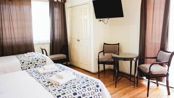 Habitación de hotel con dos camas, un escritorio, una silla y un televisor instalado en la pared.