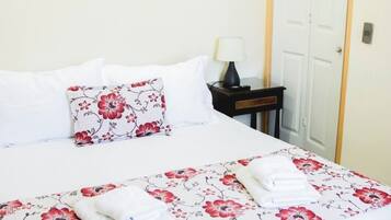 A neatly made bed with floral bedding, a bedside table with a lamp, and a door with a light switch.