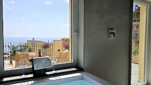 Ein Badezimmer mit einer Badewanne, einem Fenster mit Blick auf das Meer und Gebäude sowie einem Handtuchhalter mit Handtuch und Weinglas.