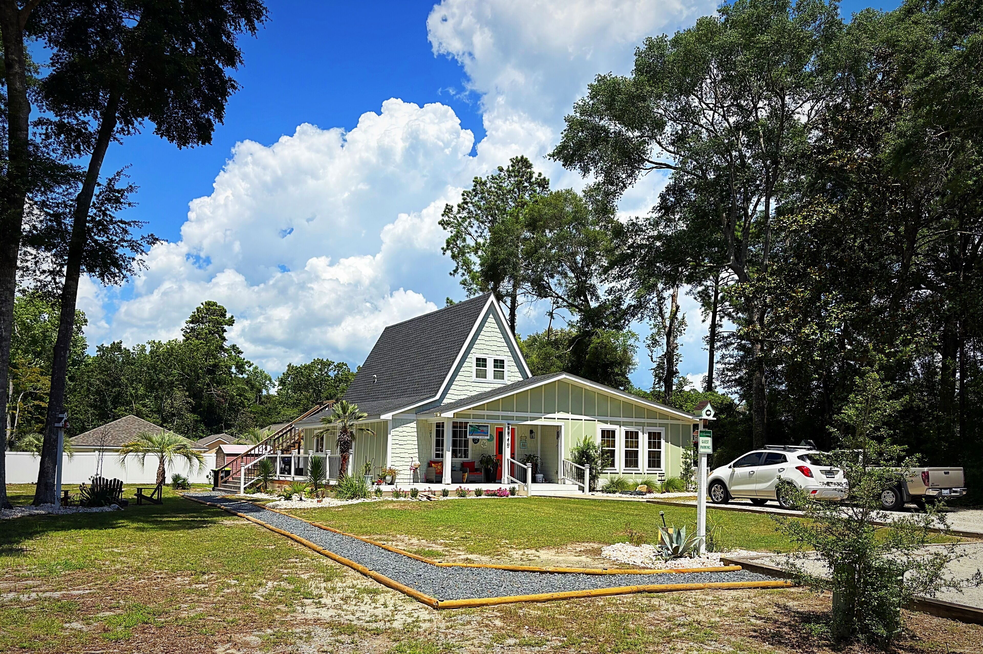 A two-story house with a front porch, a driveway, and a parking area with cars.