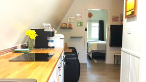 Una cocina compacta con encimera de madera, un lavamanos y un horno negro. Hay una zona de comedor con un banco y una mesa, y una puerta que da a otra habitación.