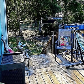 Una terraza de madera con vista a un río, una silla con un cojín colorido y un letrero que dice 'CYCLE LINE'.