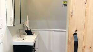 Un baño pequeño con un lavamanos blanco, un espejo y una puerta de madera.