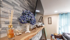 Un salon avec un mur en pierre, une étagère en bois ornée d’objets décoratifs, un canapé et une fenêtre avec des rideaux.