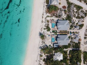 An aerial view of a beachfront property with multiple buildings, including a large house with a swimming pool and a smaller structure with a pool.