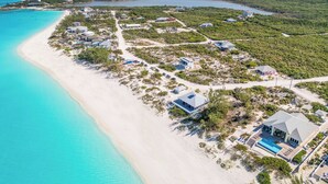 An aerial view of a coastal resort with beachfront properties, clear turquoise waters, and a mix of residential and commercial buildings. - Yumey Sands Villa, Heated Pool & Unbelievable Year-Round Calm Beach (Moore Hill)