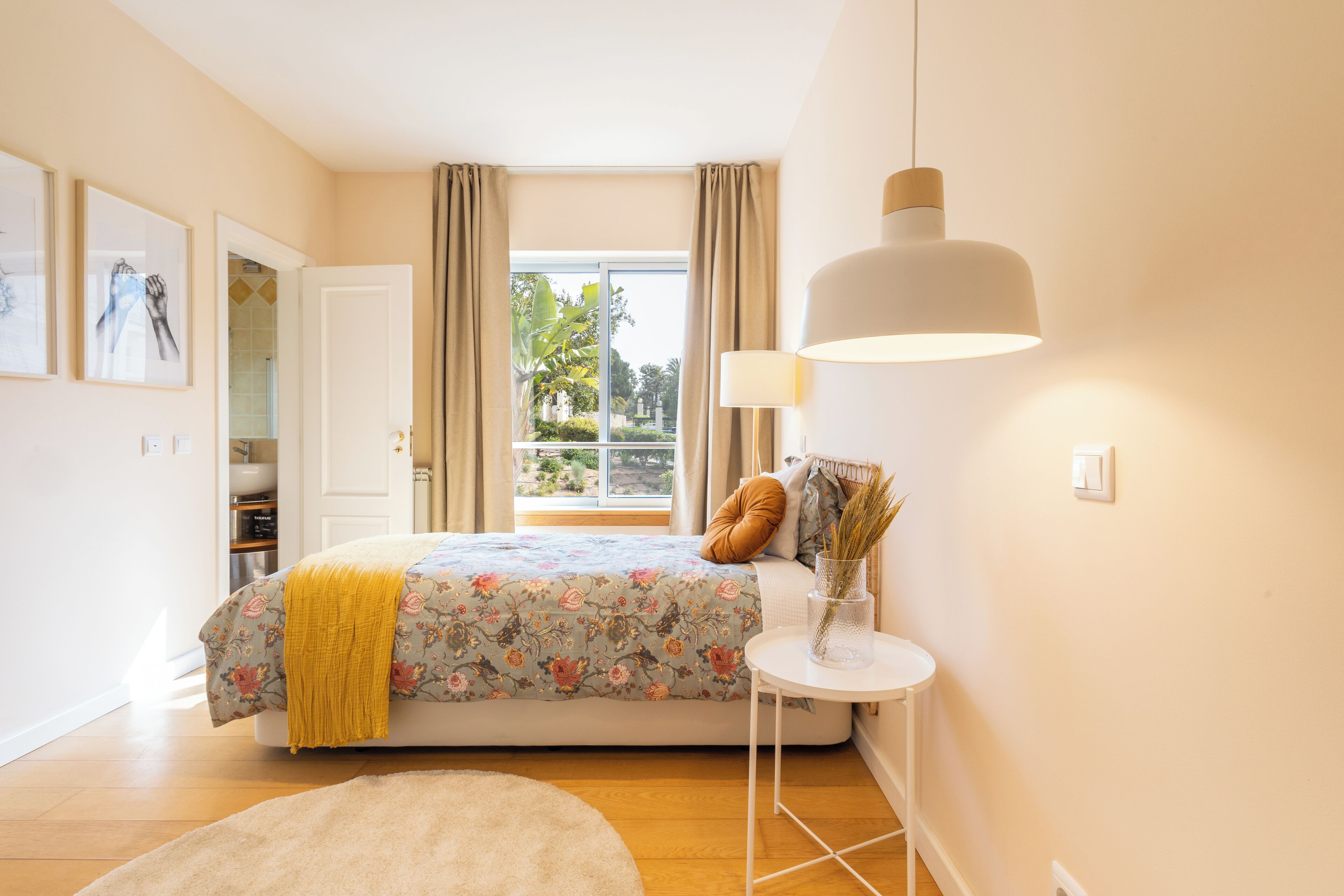 A bedroom with a bed, a bedside table, a lamp, and a view of the outdoors.