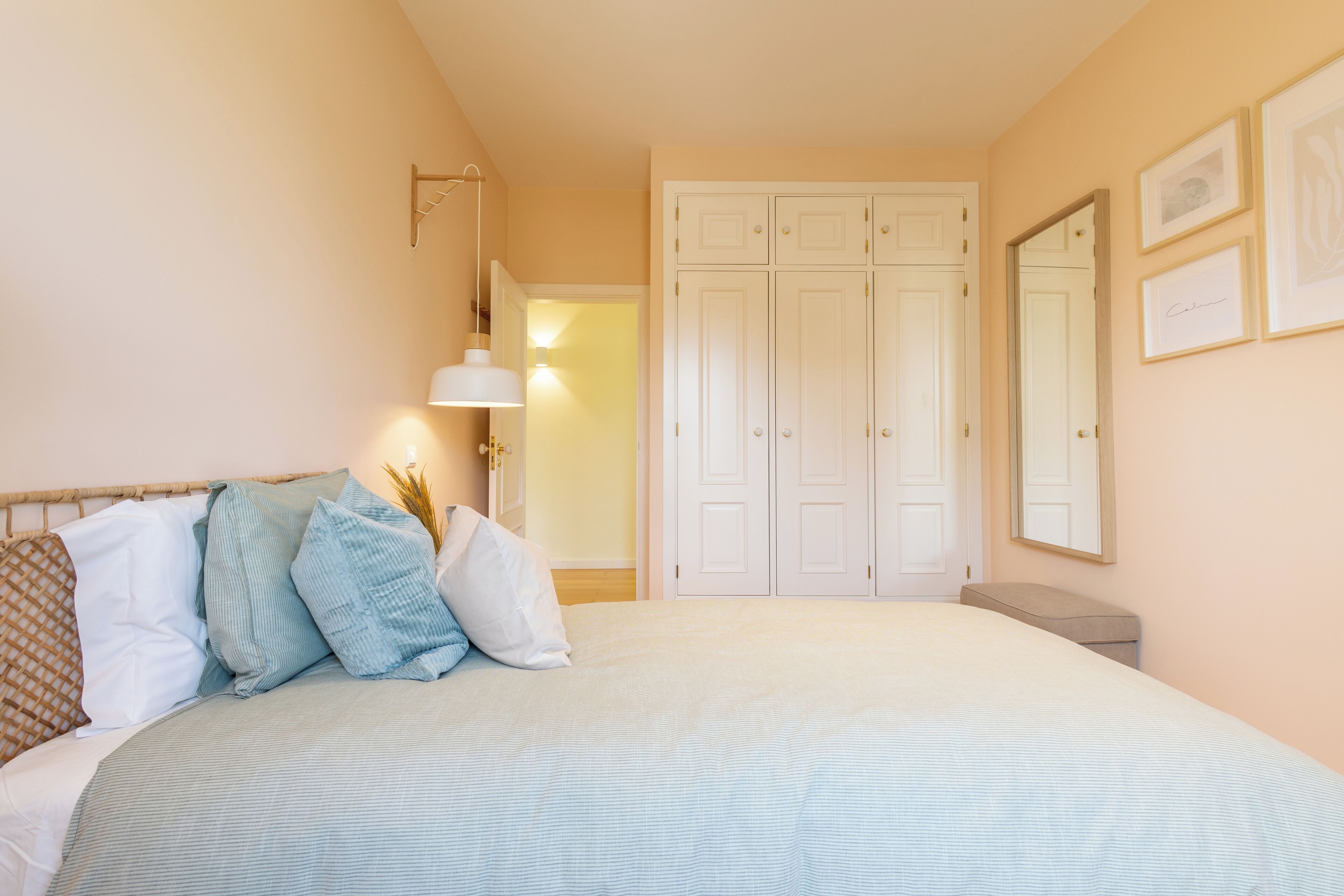 Un dormitorio con cama, armario, lámpara de noche y cuadros en la pared.