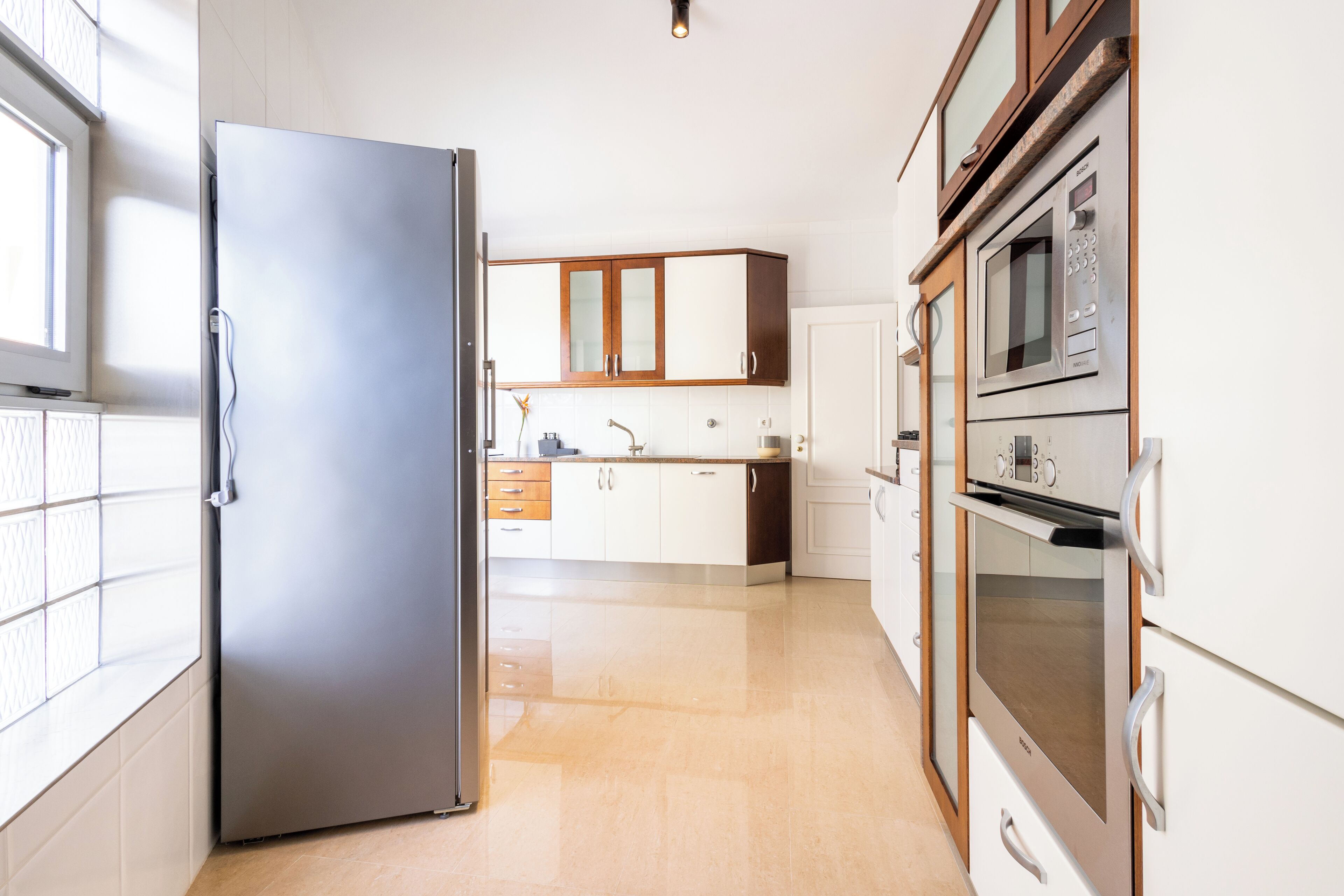 Una cocina moderna con refrigerador de acero inoxidable, armarios de madera, horno empotrado y microondas.
