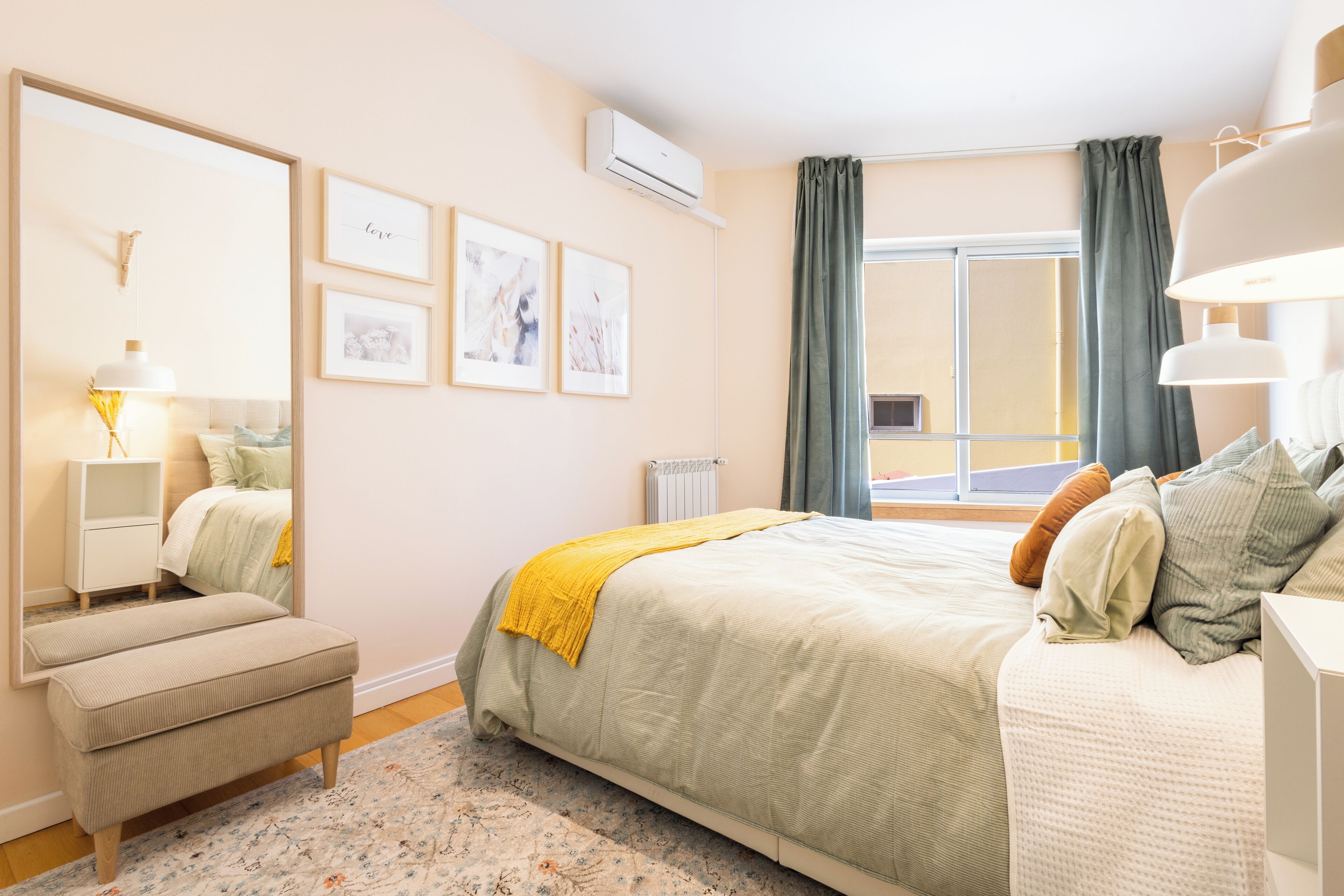 Une chambre à coucher comprenant un lit, une table de chevet, un miroir, une commode et une fenêtre avec des rideaux.