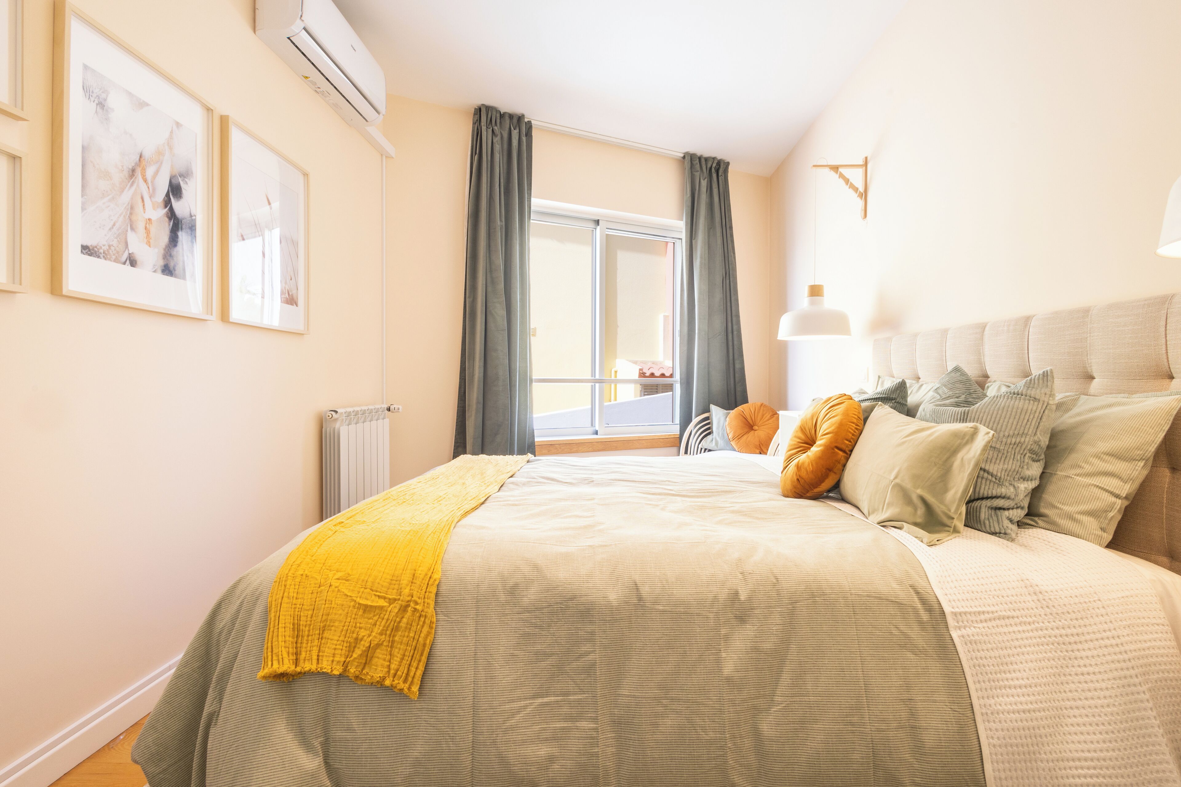Een slaapkamer met een groot bed, een radiator, een raam met gordijnen en kunstwerken aan de muur.