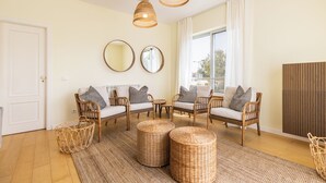 Un salon doté de meubles en osier, d’une grande fenêtre et offrant une vue sur l’extérieur.