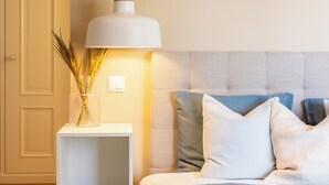 Une chambre à coucher bien rangée, avec un lit, une table de chevet dotée d’une lampe et un luminaire fixé au mur.