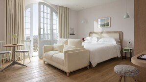 A hotel room with a bed, a sofa, a small table, a chair, and a view of the outdoors. - Auberge La Coste (Le Puy-Sainte-Reparade)