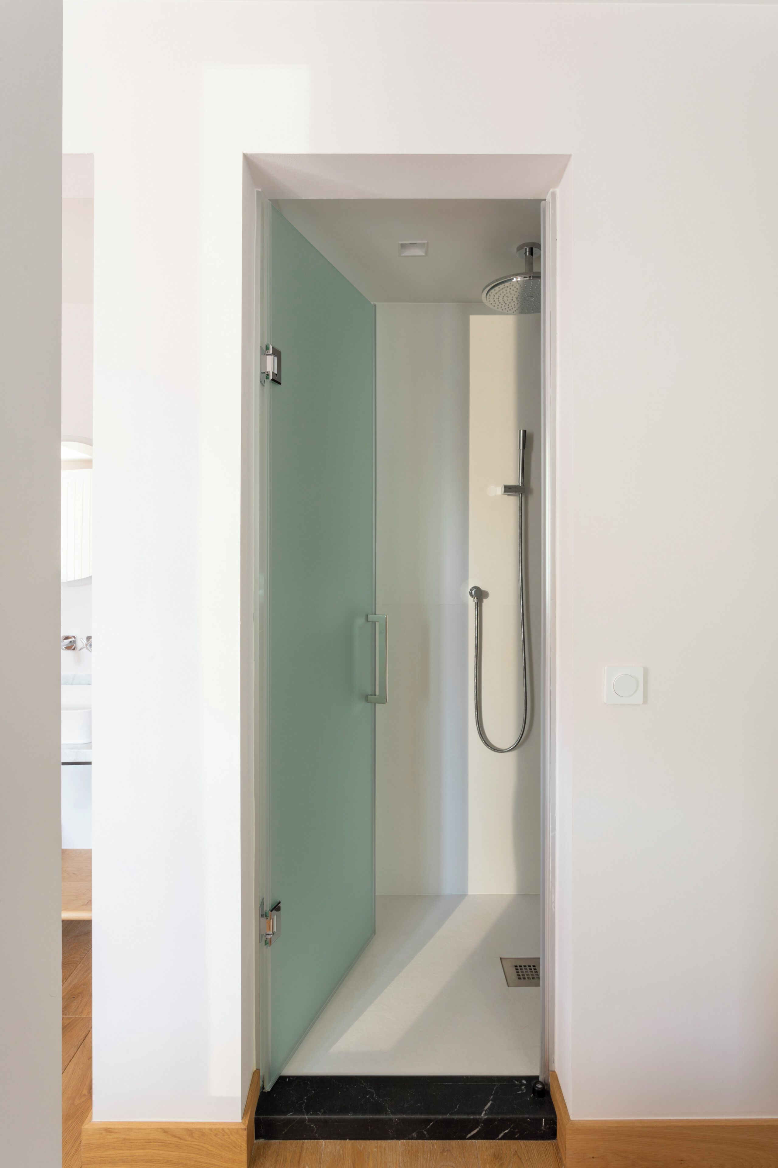 A narrow doorway leading to a shower area with a handheld showerhead and a wall-mounted faucet.